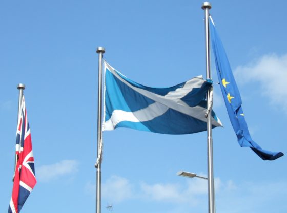 Flags outside the Scottish Parliament in Edinburgh, Scotland. Left to right: British flag, Scottish flag, European Union flag. The Scottish flag is unfurled. The others hang limply by their flagpoles.