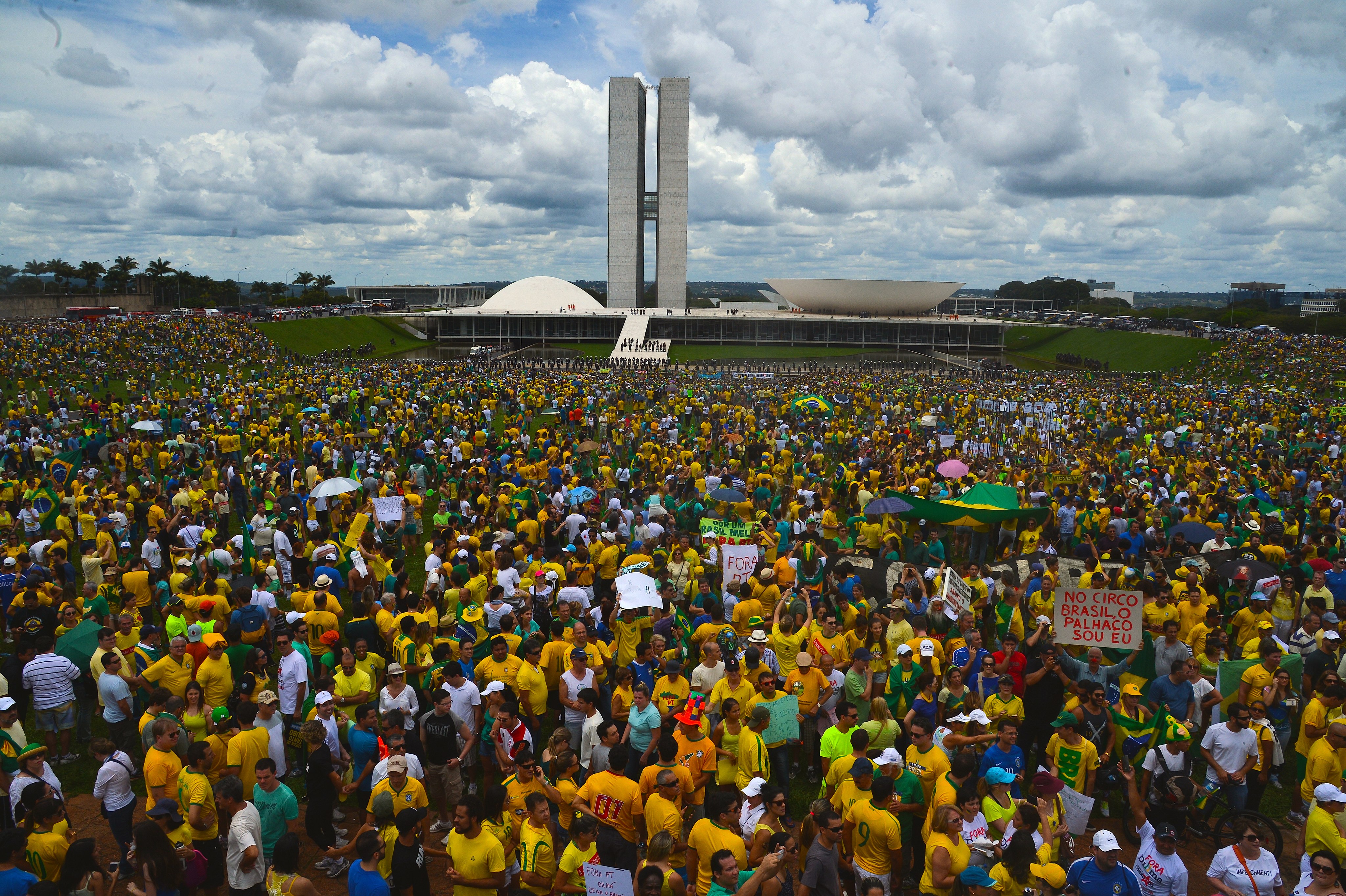 A large crowd of anti-corruption protesters dressed predominantly in the yellow and green of the Brazilian flag stands in front of the Congresso Nacional, designed by Oscar Niemeyer, in Brasilia, Brazil.